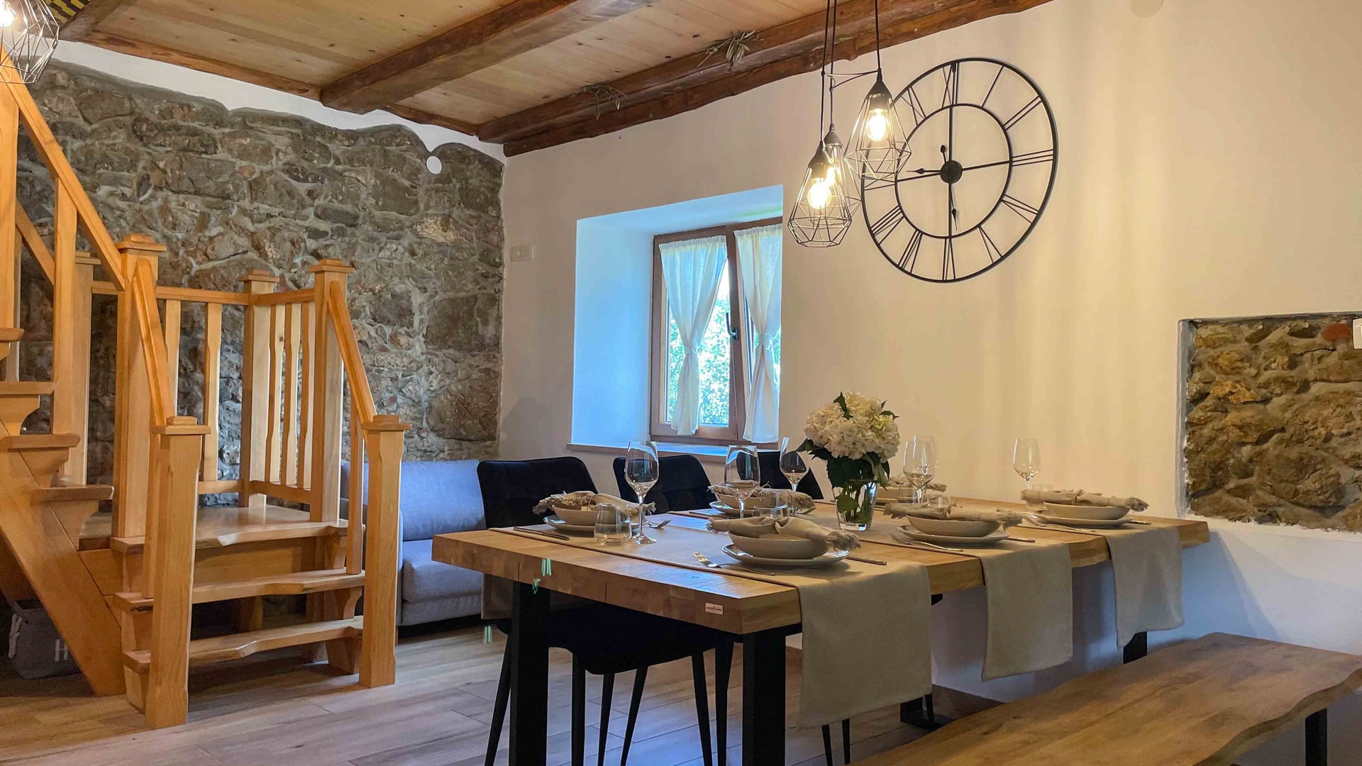 Kuća Amalia – blagovaonica s kamenim zidom, drvenim stubištem i satom